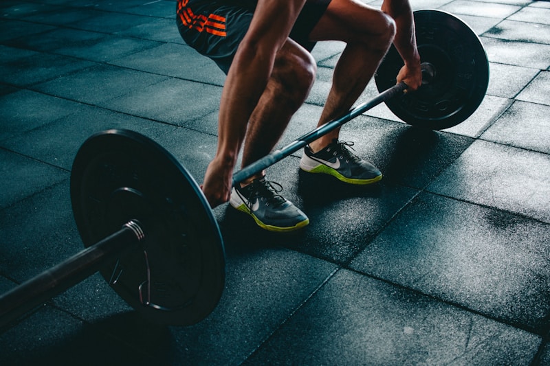 Person in tiefer Hocke beim Anheben einer Langhantel auf schwarzem Bodenbelag im Fitnessstudio